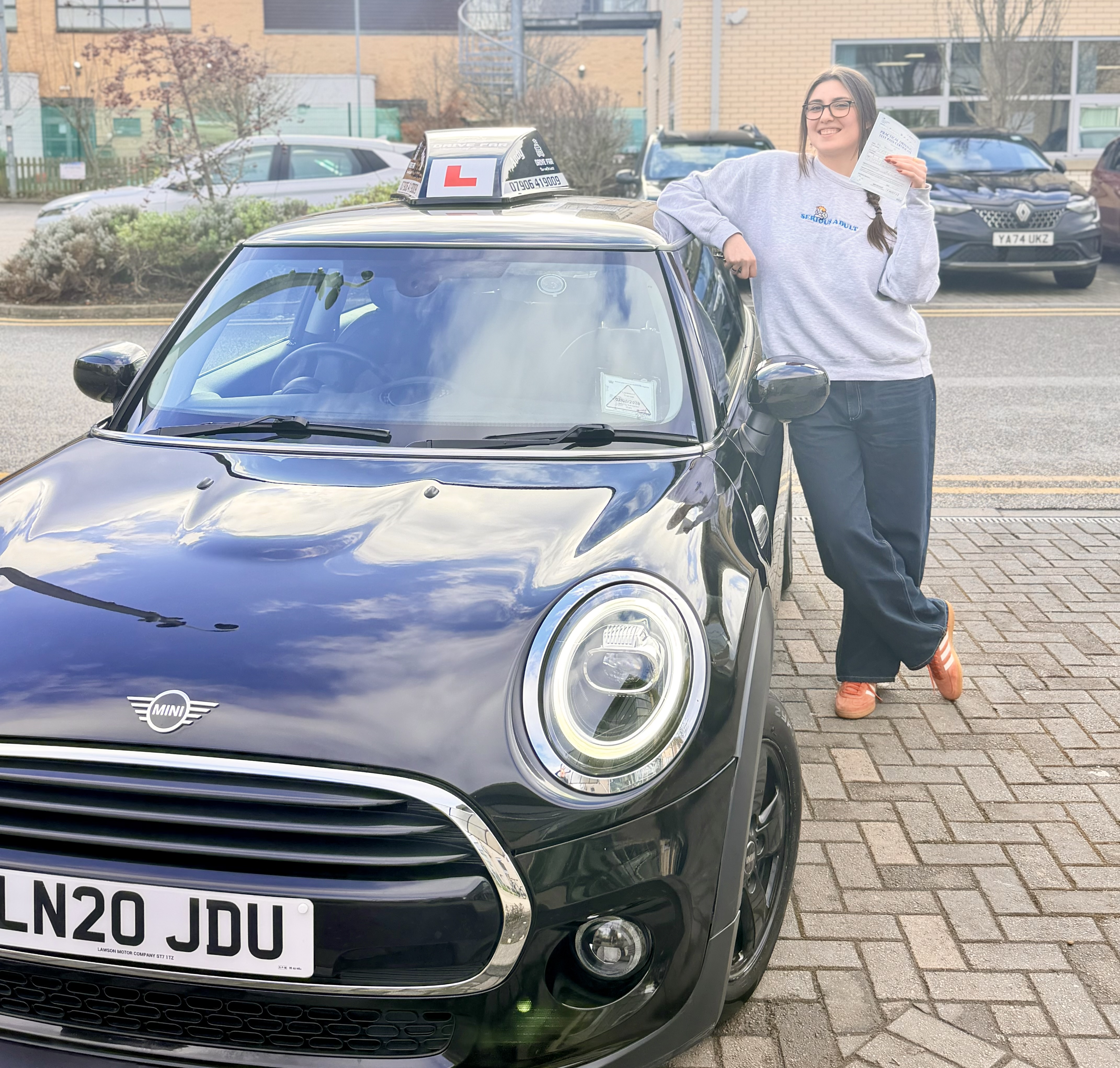 Successful learner holding her practical driving test pass certificate beside the Doodles Driving Mini