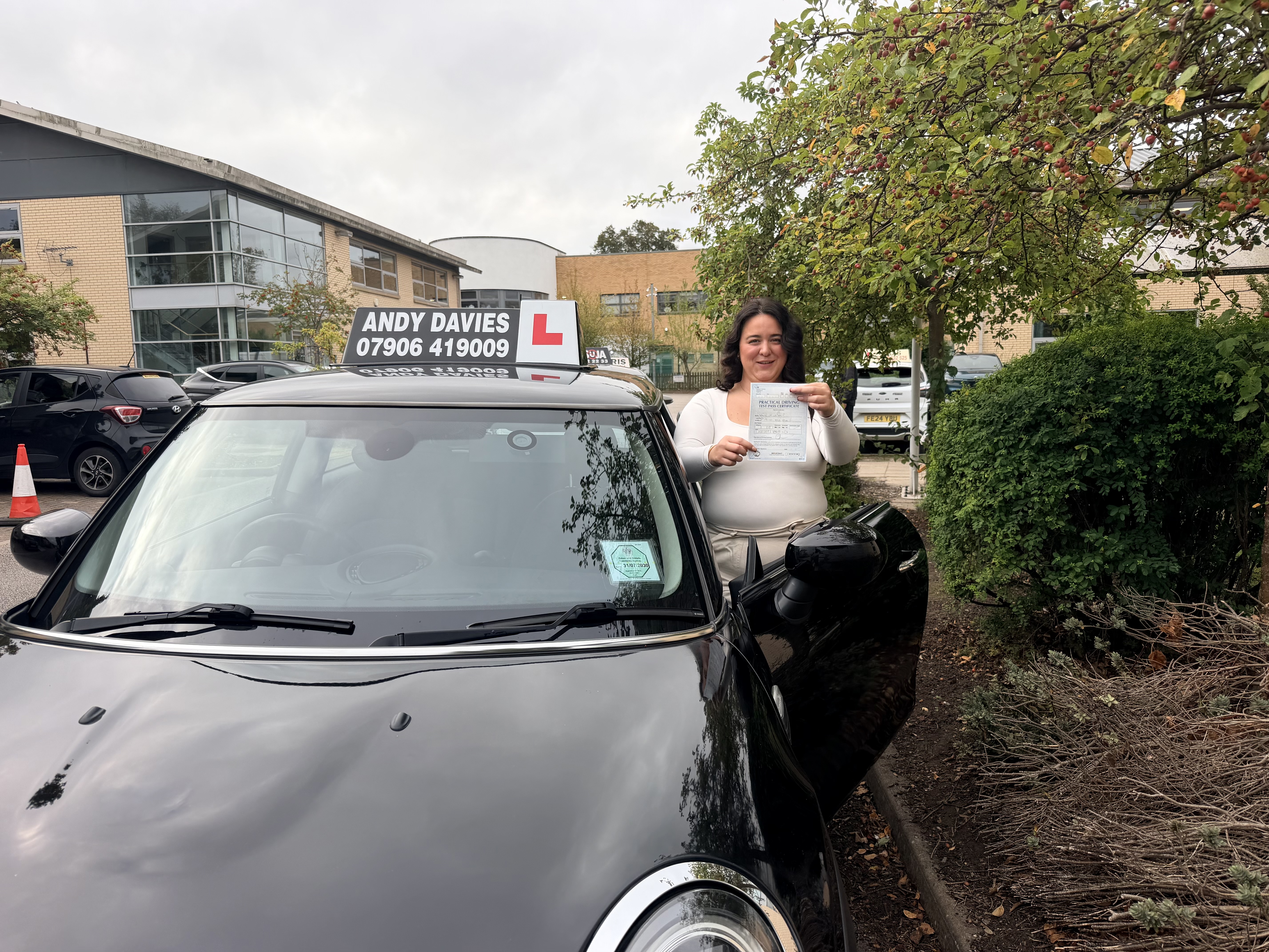 Successful learner holding her practical driving test pass certificate beside the Doodles Driving Mini